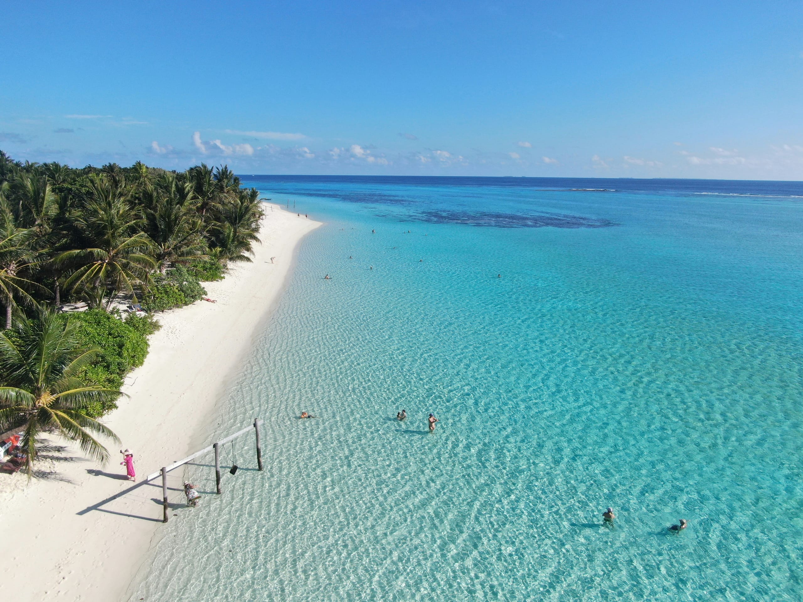 A white sand beach on a local island with a volleyball net at the waterline and people swimming in clear shallow water