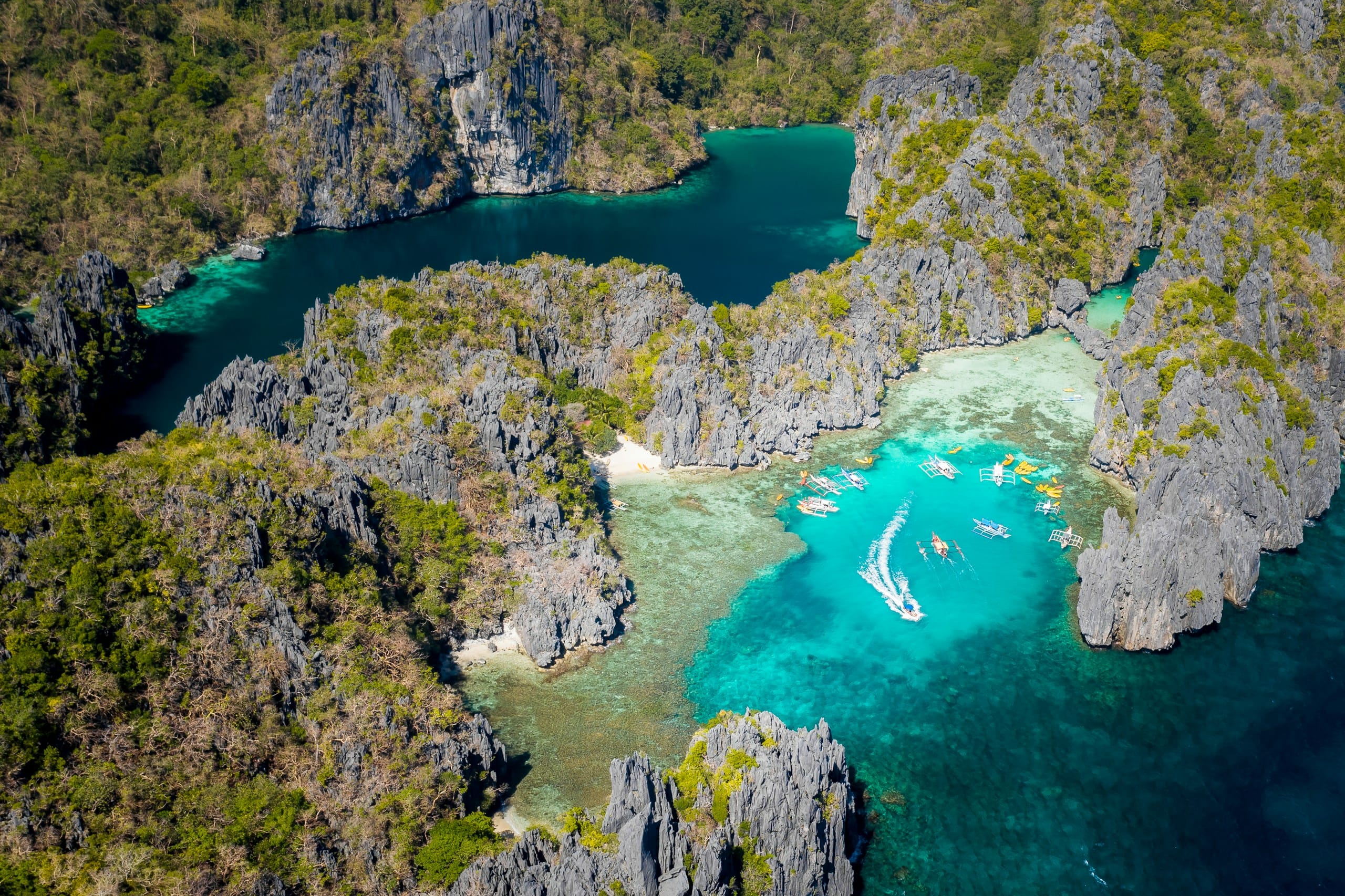 The lagoons at El Nido from the air, turquoise water held inside limestone walls with tour boats gathered at the entrance